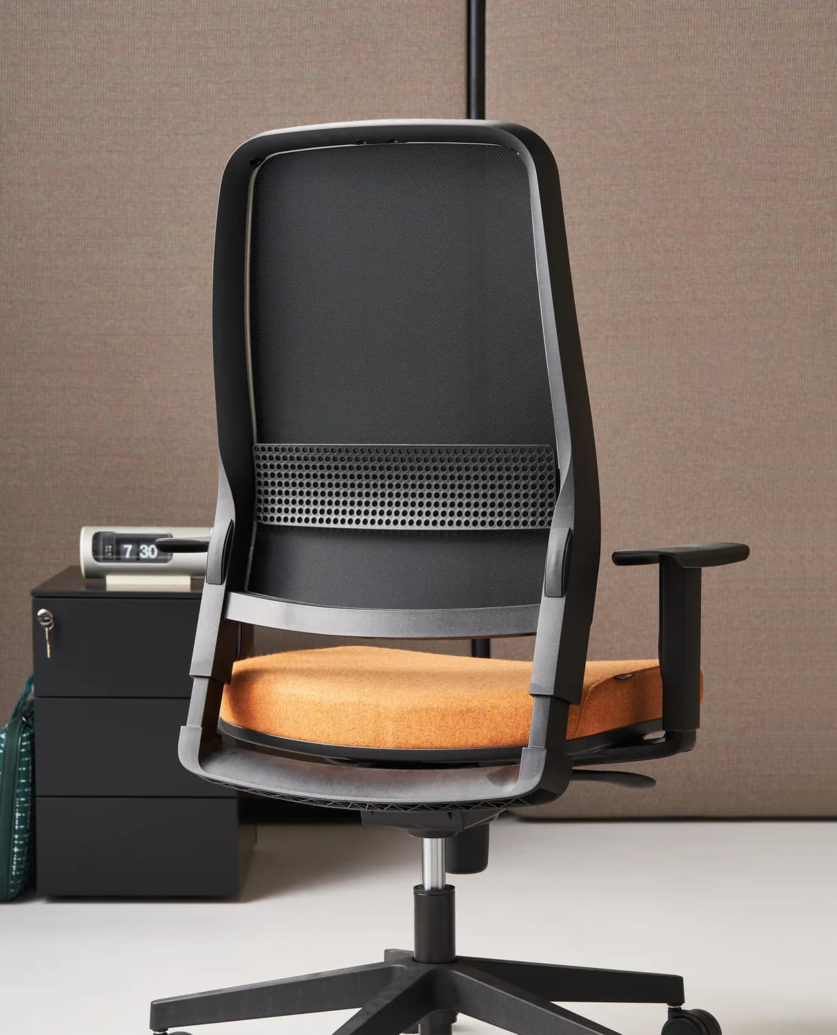 Sedute operative 505 con schienale in rete e sedile arancio, su un open space con postazioni bianche e parete decorata