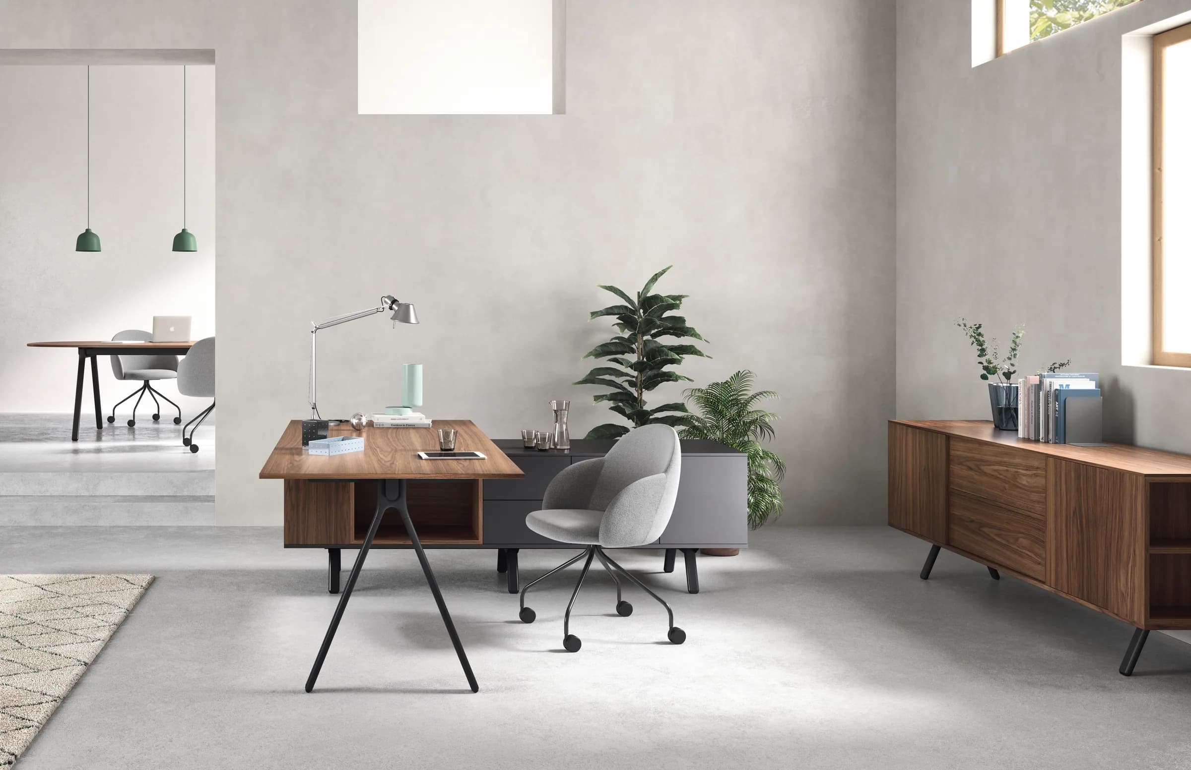 Ufficio direzionale Alter in noce con gamba a cavalletto, contenitore portante antracite, poltroncina grigia, madia in legno e piante.