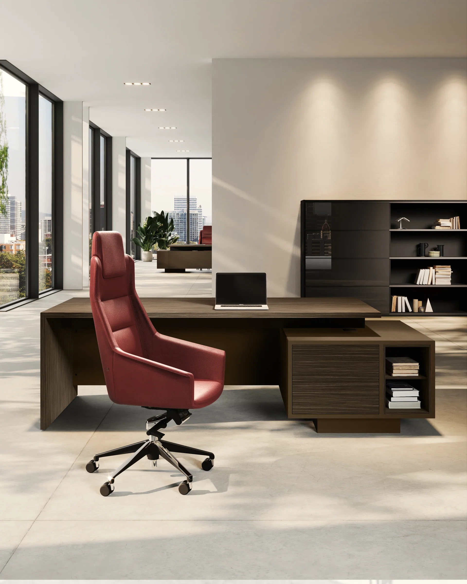 Ufficio direzionale Gotha in essenza scura: scrivania con fianco a pannello e giunzione a 45°, mobile di servizio portante con cassettone e vano a giorno, poltrona in pelle rossa. A destra contenitore alto con ante in vetro fumé e libreria; sullo sfondo vetrata sulla città.