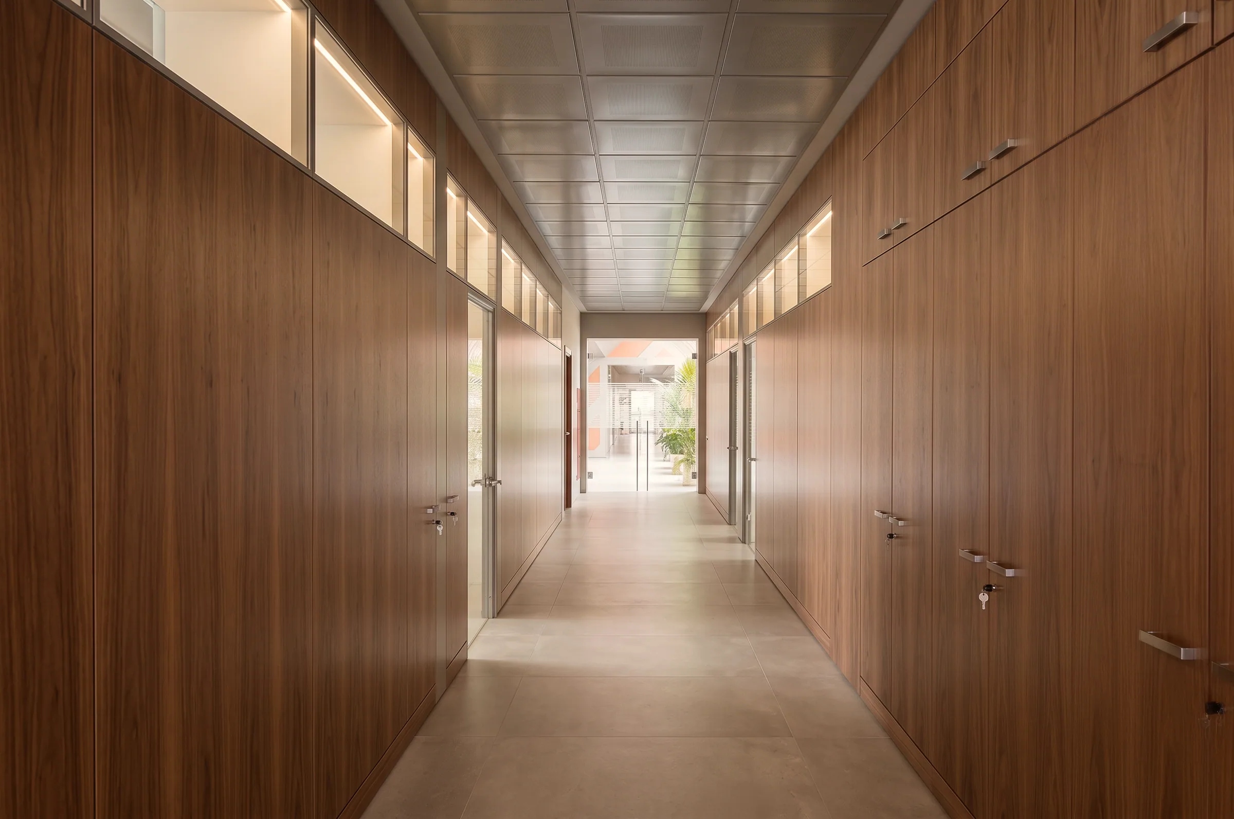 Parete divisoria attrezzata con armadiature integrate in legno, sopraluce vetrati e porte coordinate negli uffici.