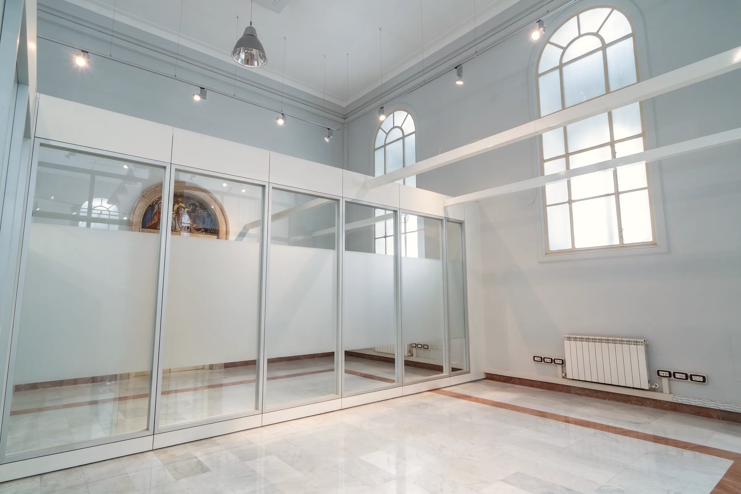 Parete divisoria vetrata con fascia satinata, profili chiari e sopraluce, inserita in ambiente storico luminoso.