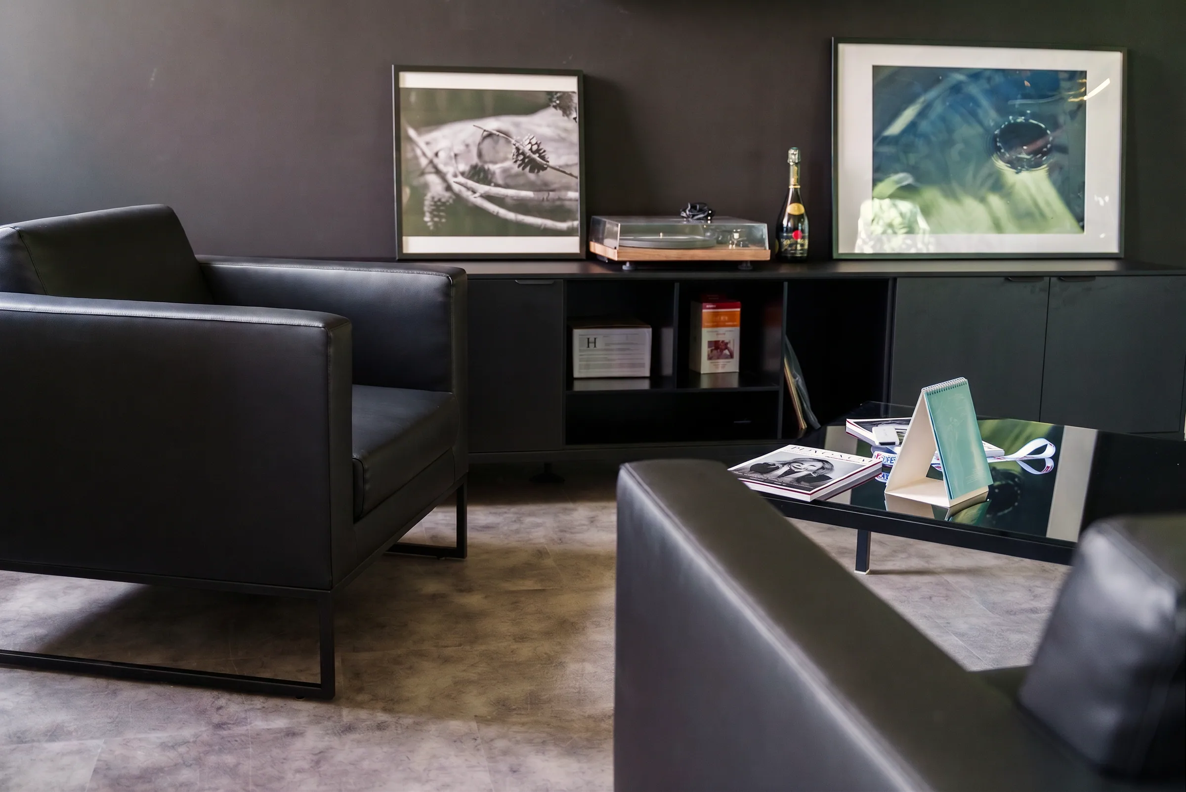 Salotto con poltrone in pelle nera, credenza bassa e quadri appesi