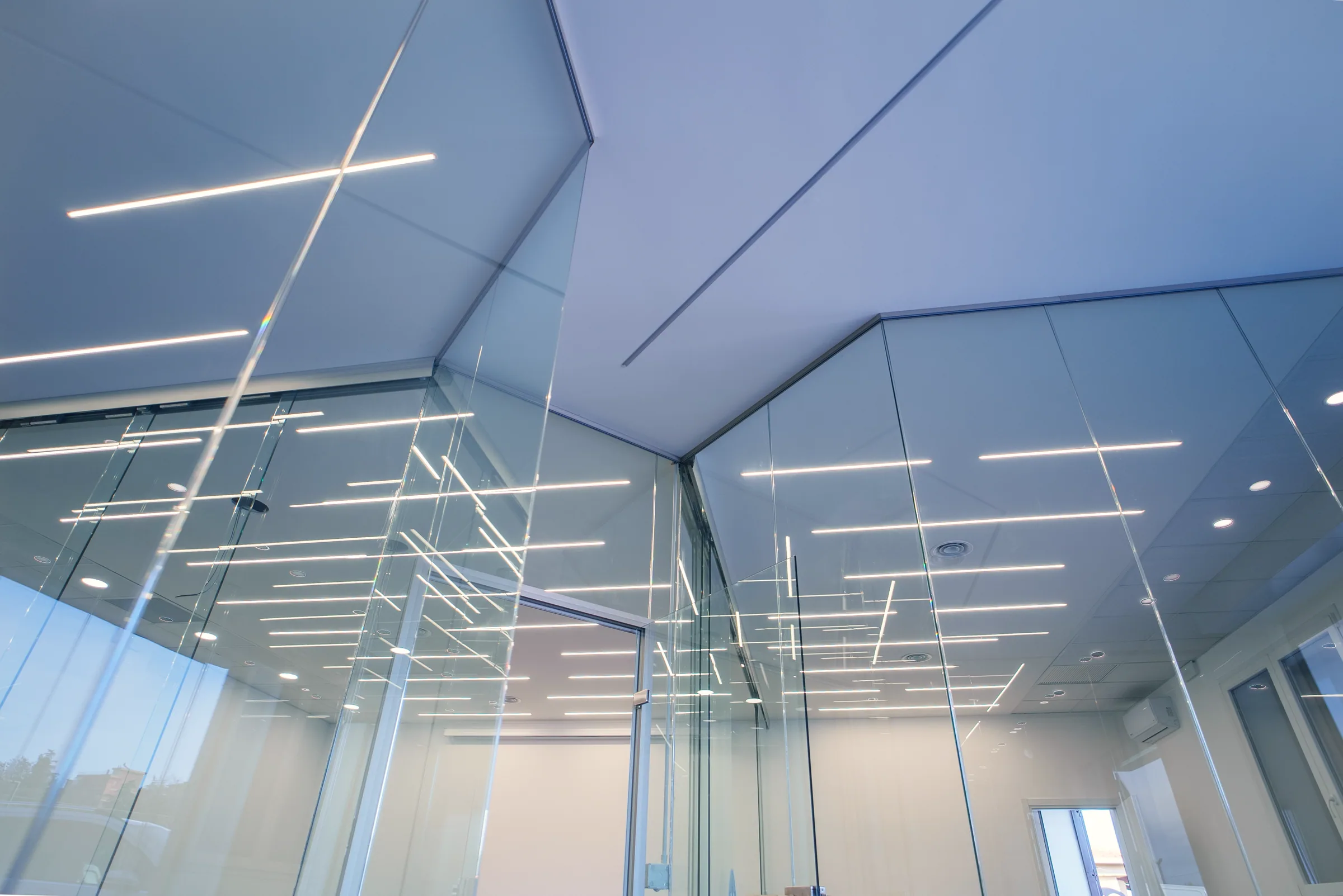 Controsoffitto sfaccettato con led lineari, visto dal basso attraverso le pareti in vetro delle aule