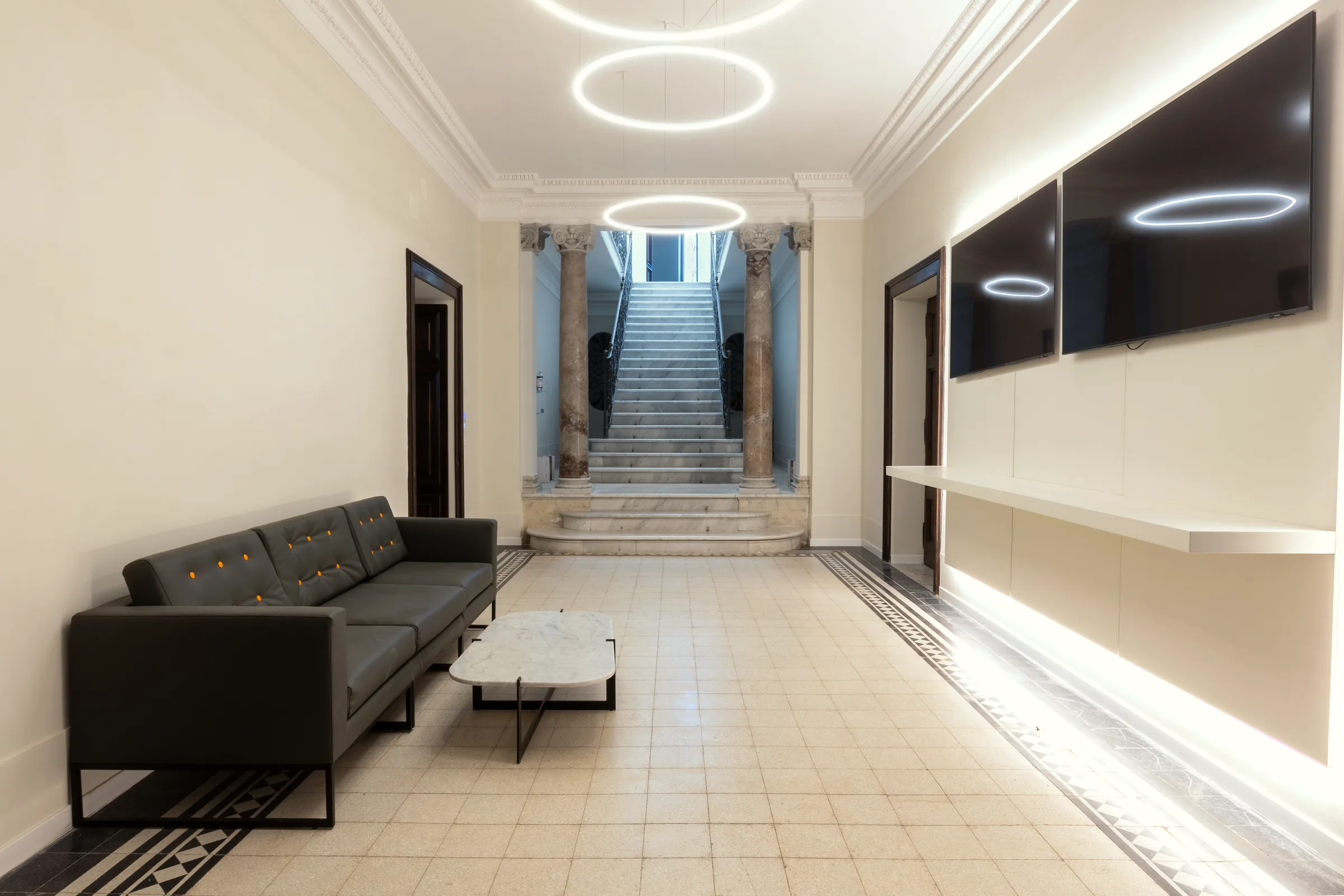 Atrio con scalone in marmo, divano scuro, tavolino e boiserie nera con anelli luminosi